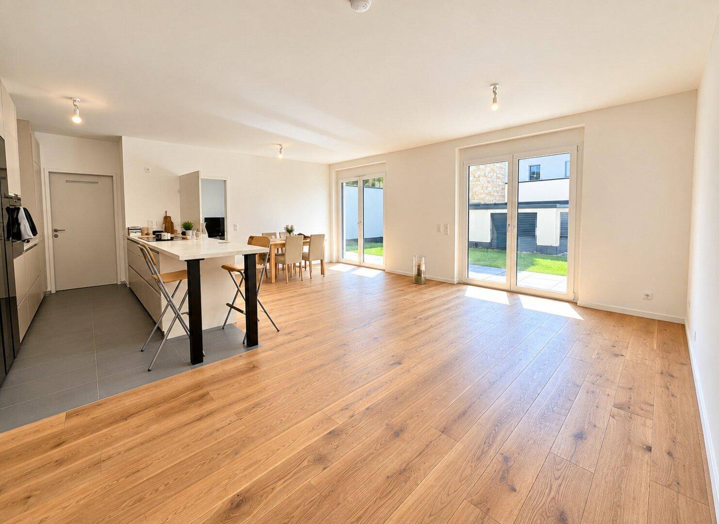 Heller offener Wohn-Essbereich mit Holzboden und Zugang zum Garten durch große Schiebetüren.