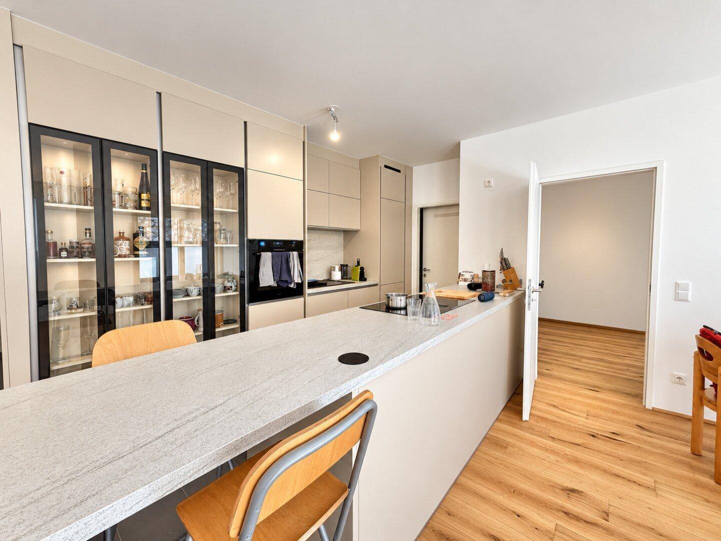 Moderne Küche mit Kücheninsel, integrierten Geräten und eleganten Glasvitrinen.