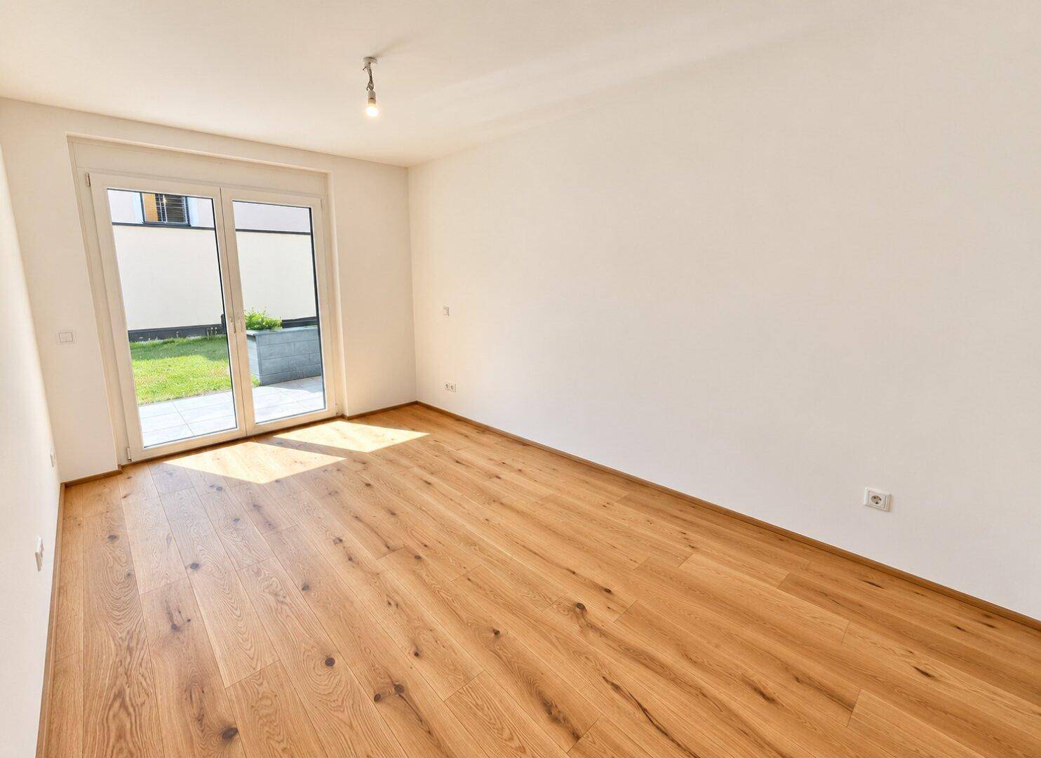 Lichtdurchfluteter Raum mit Holzboden und direktem Zugang zu einer kleinen Rasenfläche im Freien.