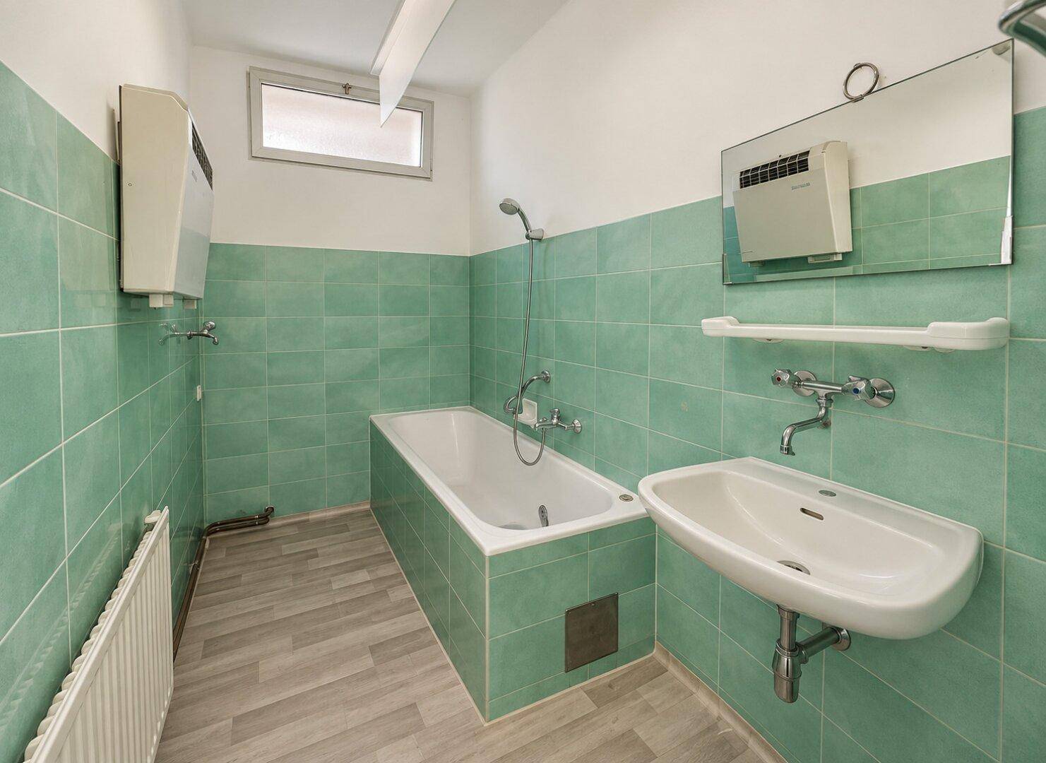 Badezimmer mit grünen Wandfliesen, Badewanne mit Duschfunktion und einem kleinen Fenster.