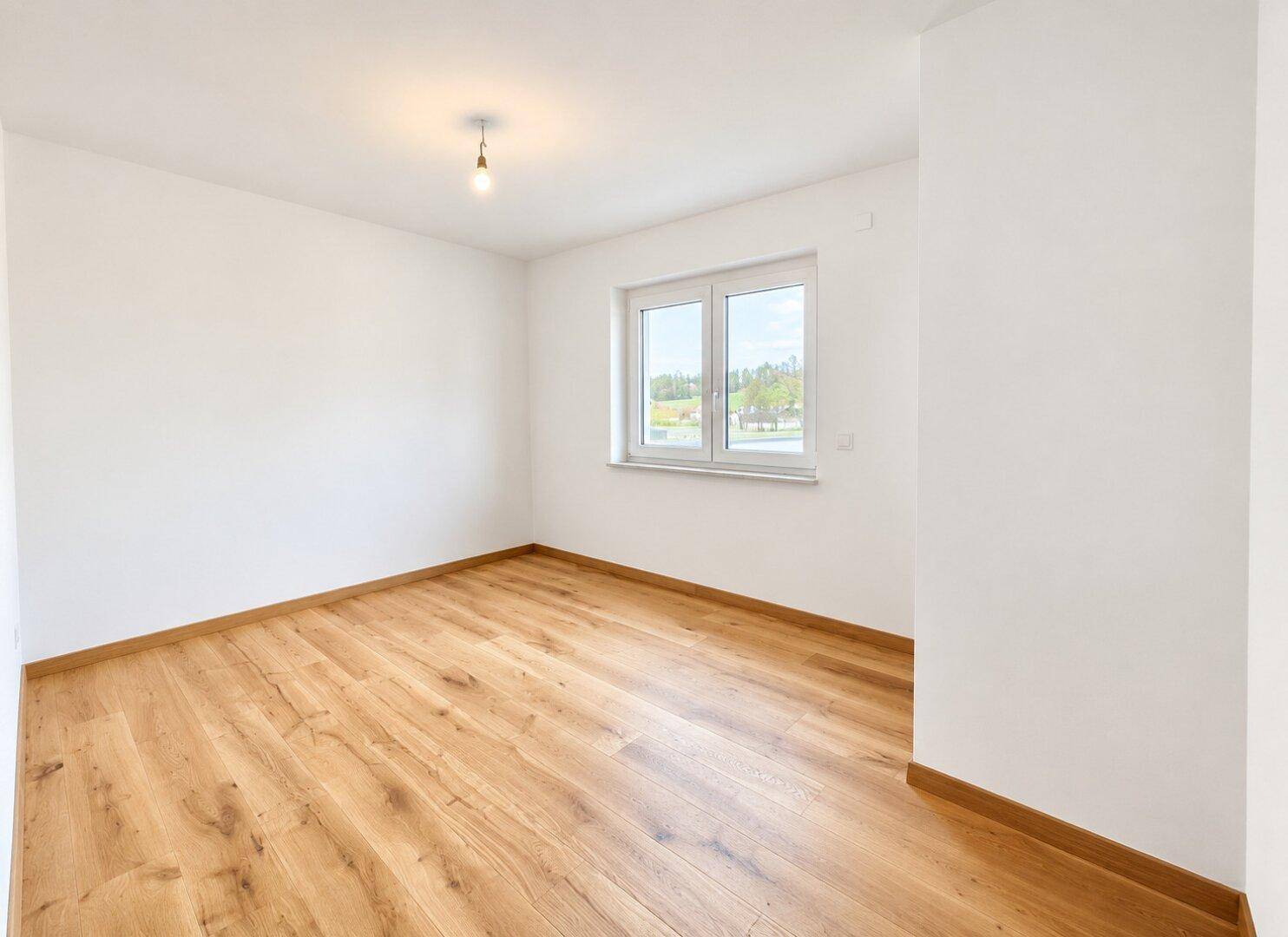 Helles, leeres Zimmer mit Holzboden und Fenster, ideal als Schlaf- oder Arbeitszimmer.