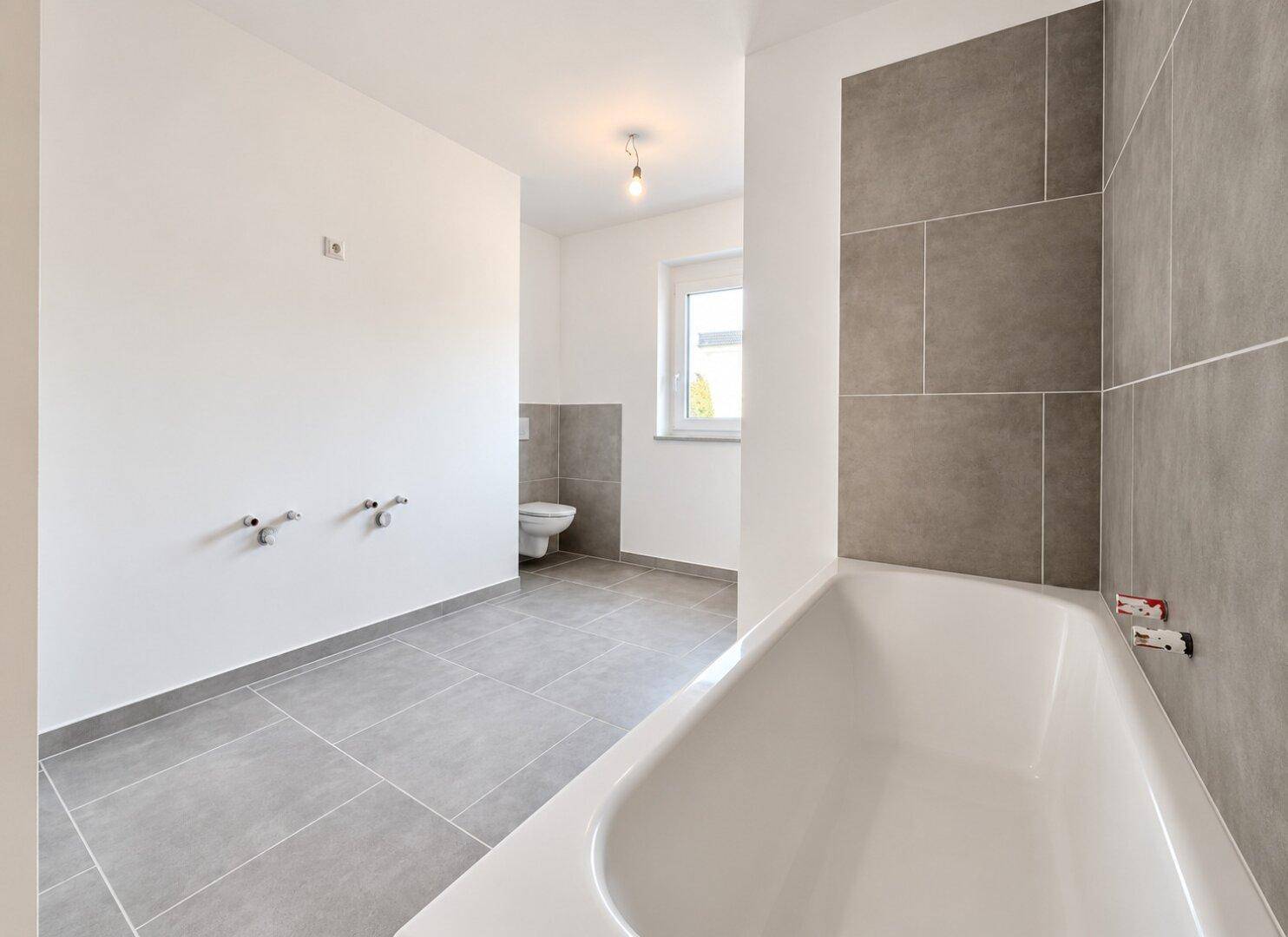 Modernes, leeres Badezimmer mit grauen Fliesen, Badewanne und wandhängendem WC.