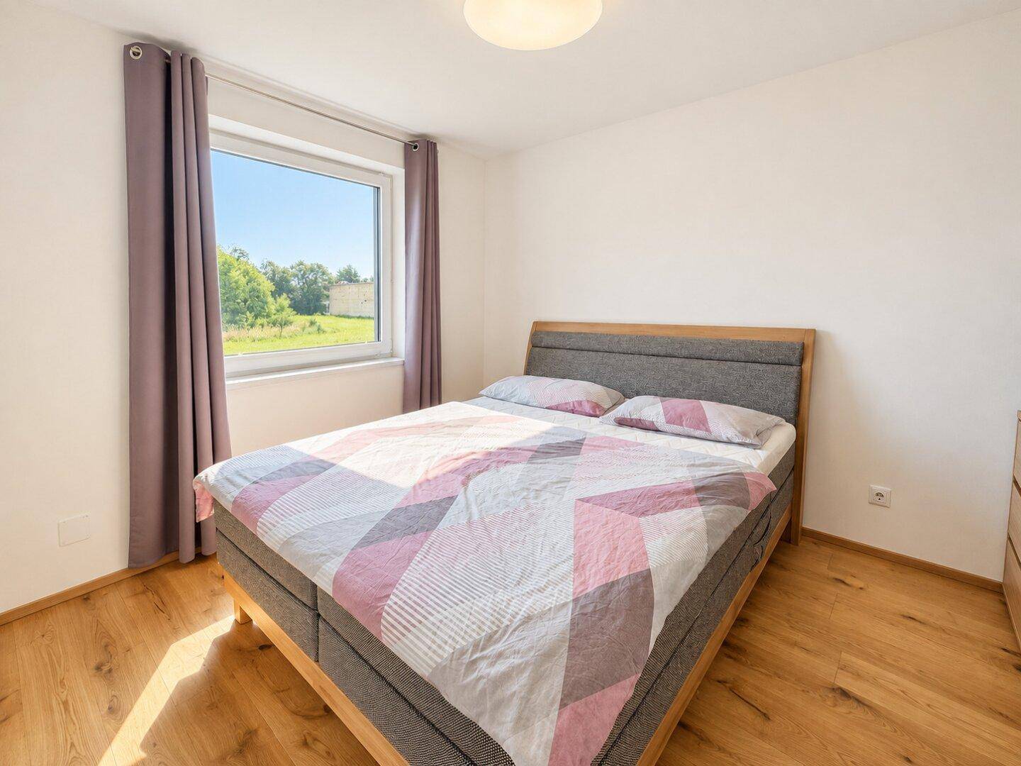 Helles Schlafzimmer mit Doppelbett und Holzboden, bietet einen ruhigen Blick ins Grüne.