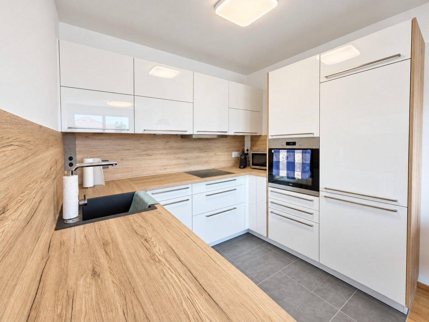 Moderne Einbauküche mit weißen Hochglanzfronten, Holz-Arbeitsplatten und integrierten Geräten.