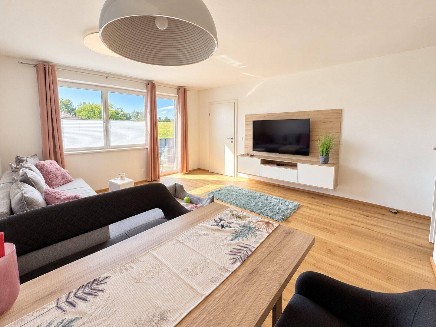 Geräumiger Wohnbereich mit TV-Möbeln, Esstisch und Zugang zu einem sonnigen Außenbereich.