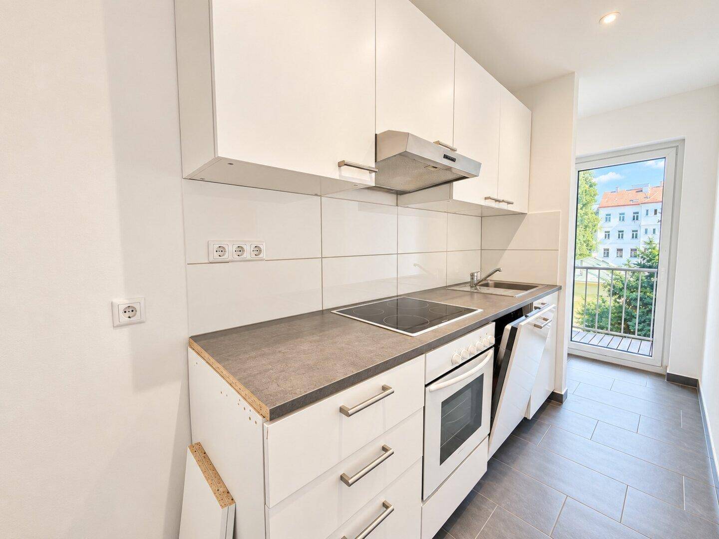 Kleine, moderne Küche mit weißen Schränken, Einbaugeräten und Zugang zum Balkon.