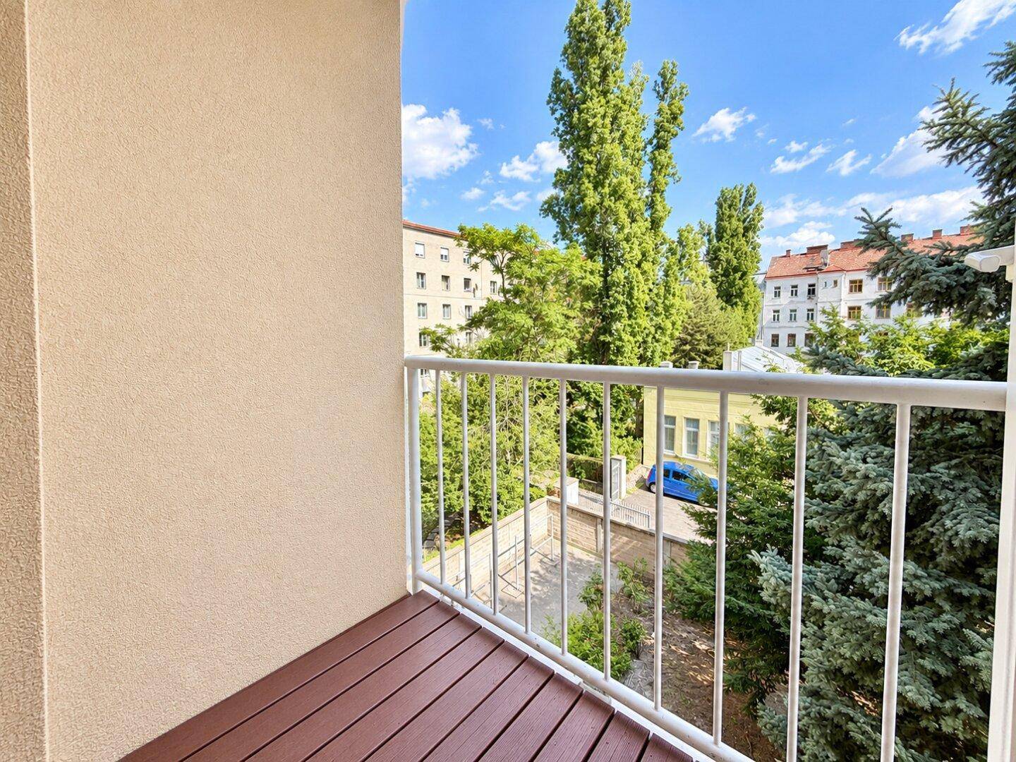 Balkon mit Holzboden und Blick ins Grüne sowie auf umliegende Gebäude.