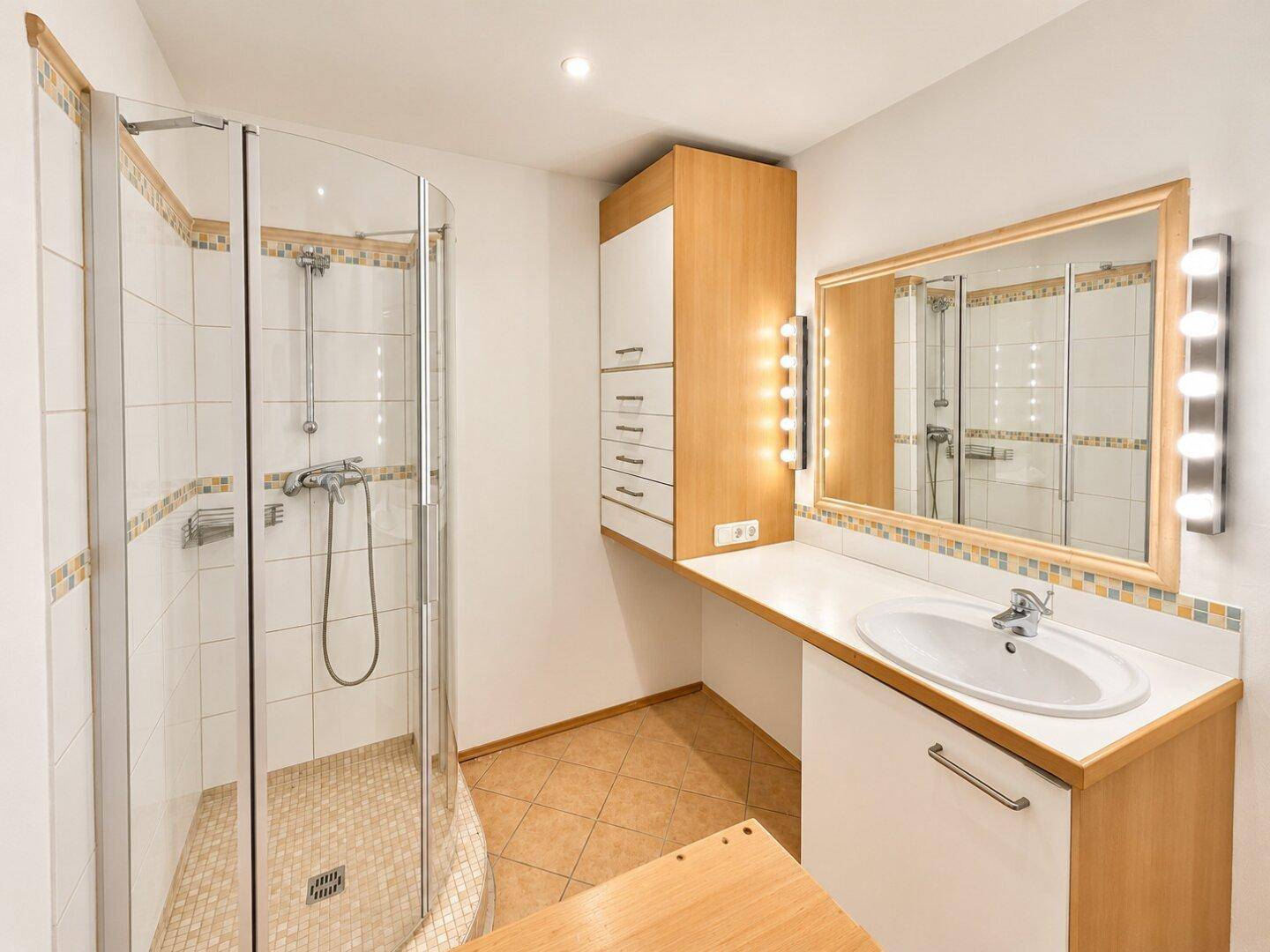 Helles Badezimmer mit Duschkabine, Einzelwaschbecken und Spiegelschrank mit Beleuchtung.