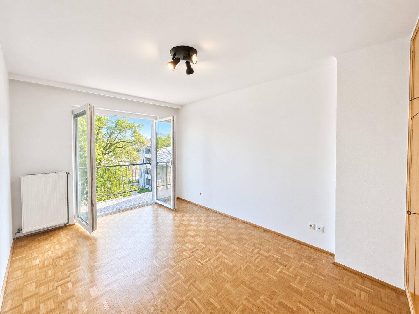 Helles, leeres Schlafzimmer mit Parkettboden und direktem Zugang zum Balkon.