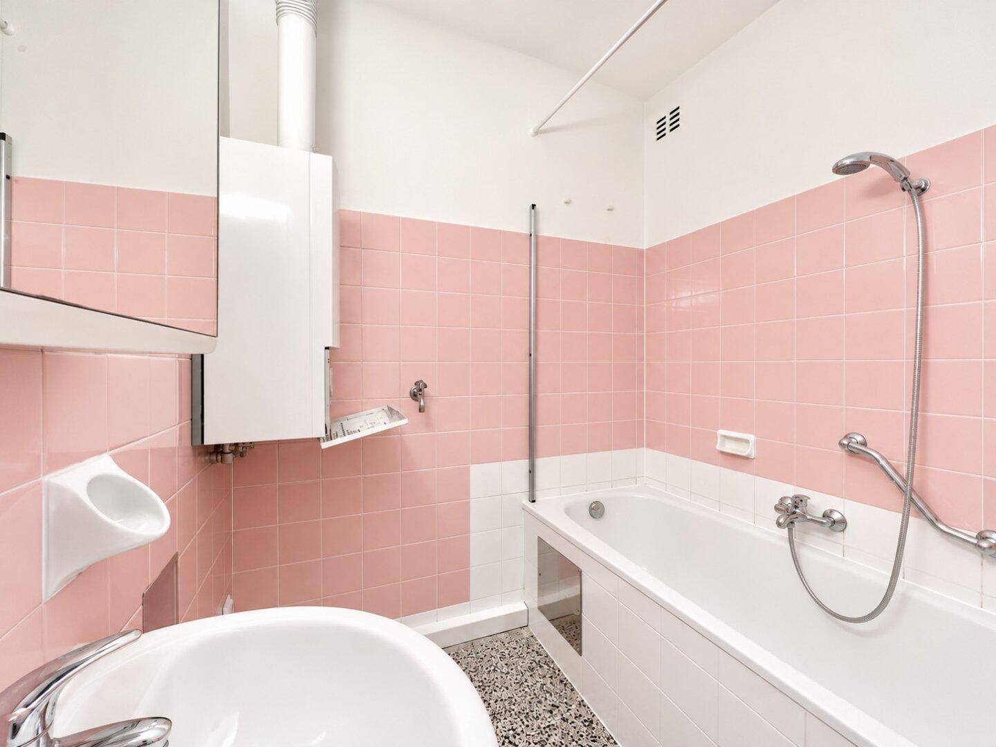 Badezimmer mit rosa Fliesen, Badewanne, Waschbecken und Haltegriffen für mehr Sicherheit.