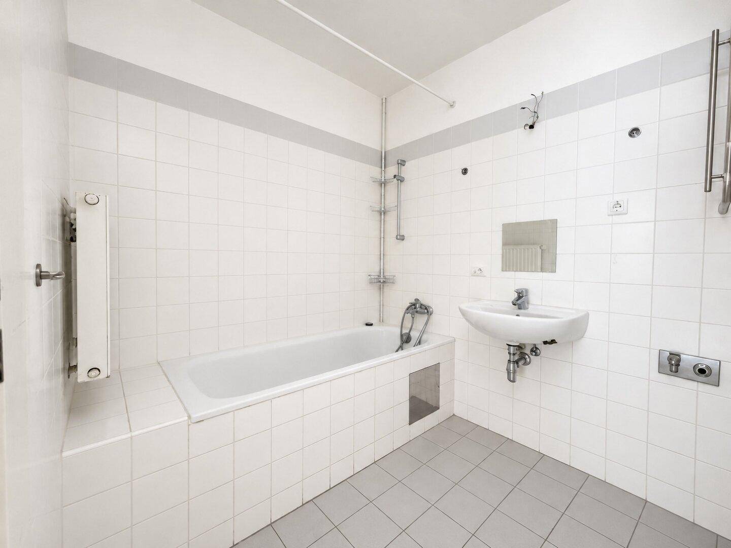 Gefliestes Badezimmer mit Badewanne, Waschbecken und beheiztem Handtuchhalter in Weiß.