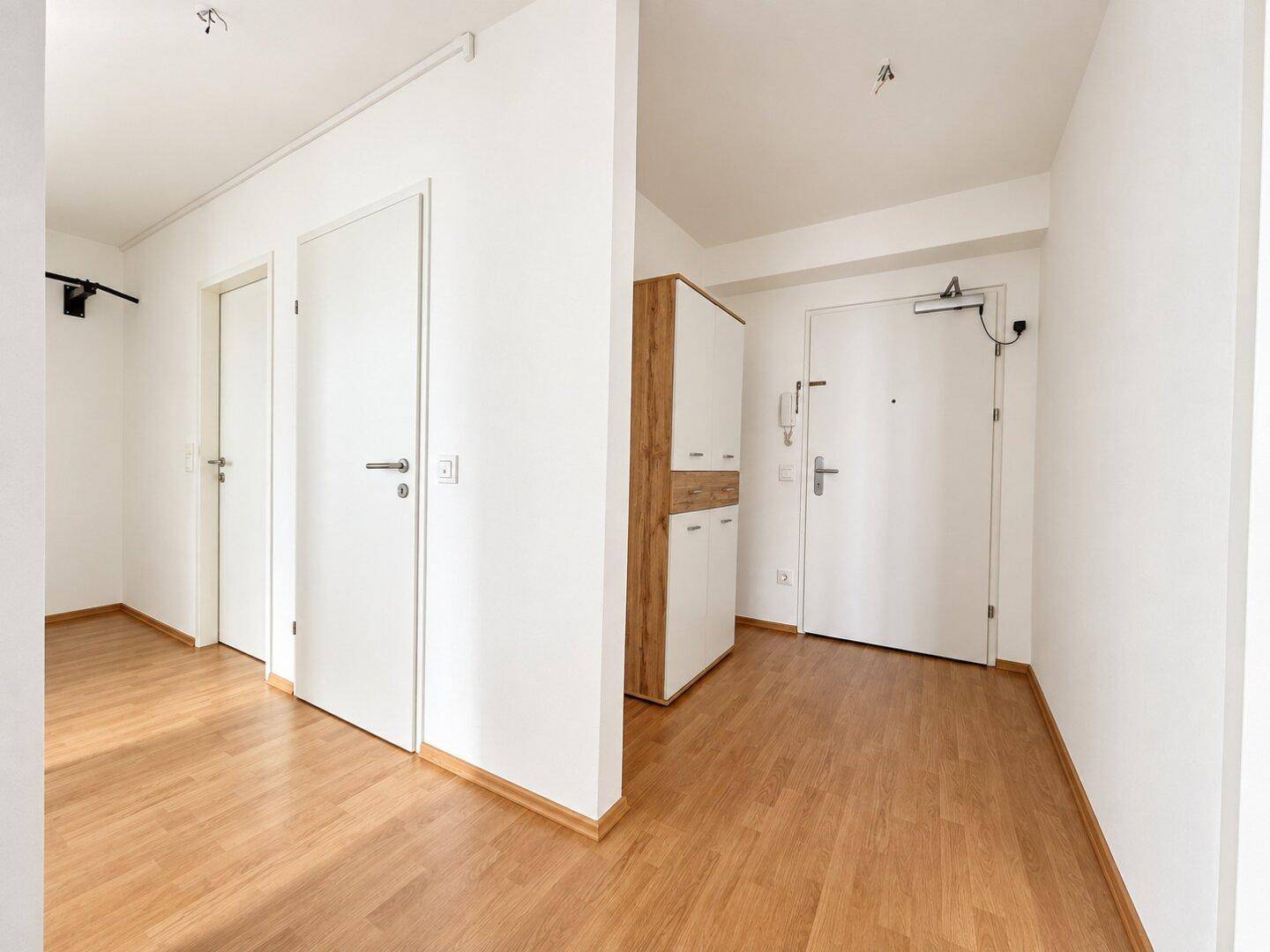 Heller Flur mit Holzboden, weißen Türen und einem modernen Garderobenschrank.