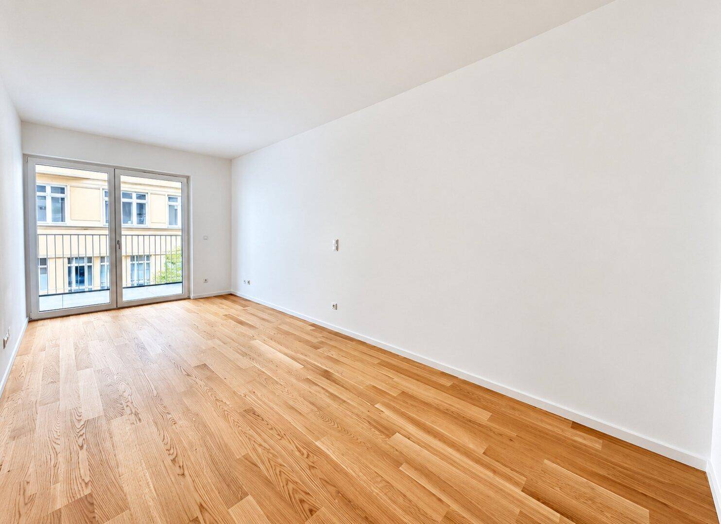 Geräumiges, leeres Schlafzimmer mit Eichenparkettboden und breiter Schiebetür zum Balkon.