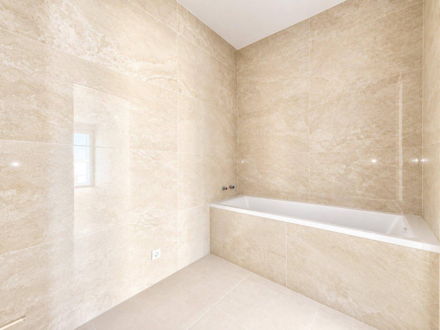 Helles Badezimmer mit beigefarbenen Fliesen und einer eingebauten Badewanne, bereit für die Installation.