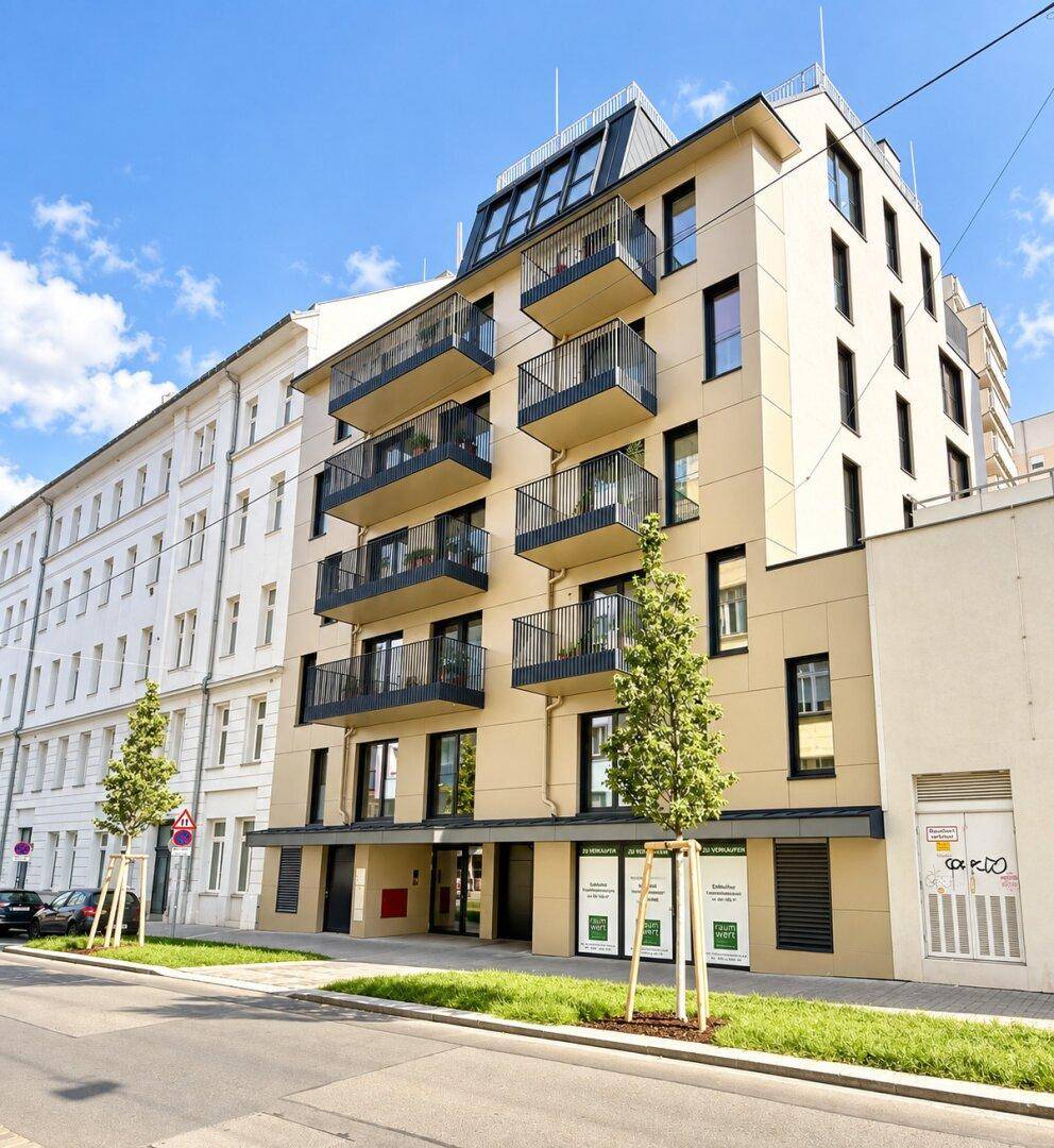 Moderne Wohnhausfassade mit mehreren Balkonen und großen Fenstern in einer städtischen Umgebung.