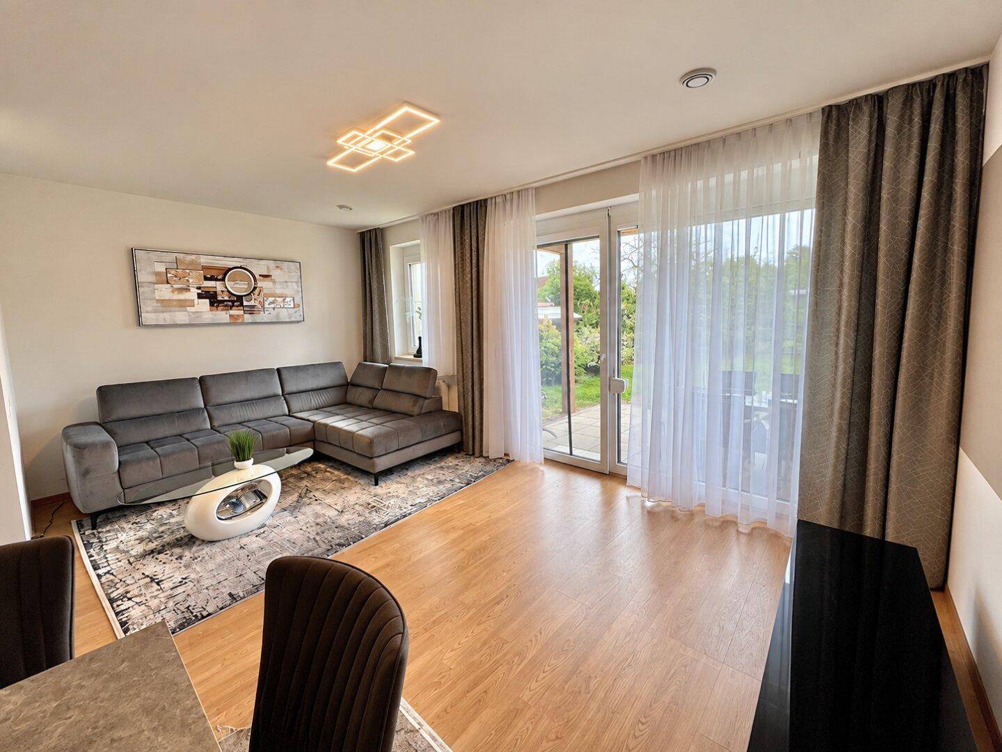 Gemütliches Wohnzimmer mit großem Sofa, Holzboden und Zugang zur Terrasse mit Gartenblick.