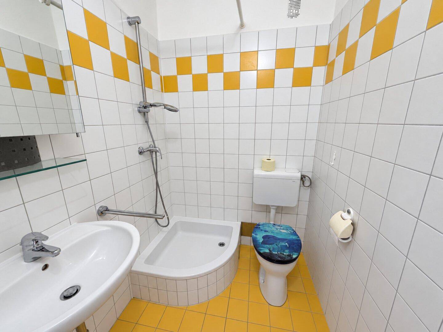 Badezimmer im 80er-Jahre-Stil mit gelb-weiß karierten Fliesen, Dusche und Einzelwaschbecken.