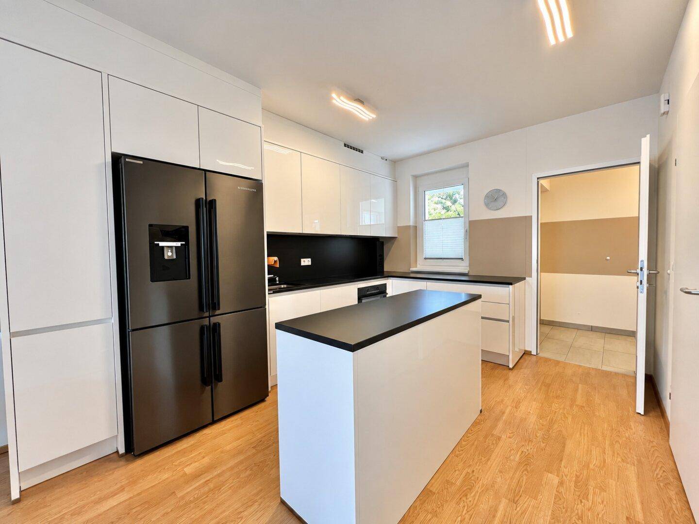 Moderne Küche mit weißen Hochglanzfronten, Kücheninsel und großem Kühlschrank, ideal zum Kochen.