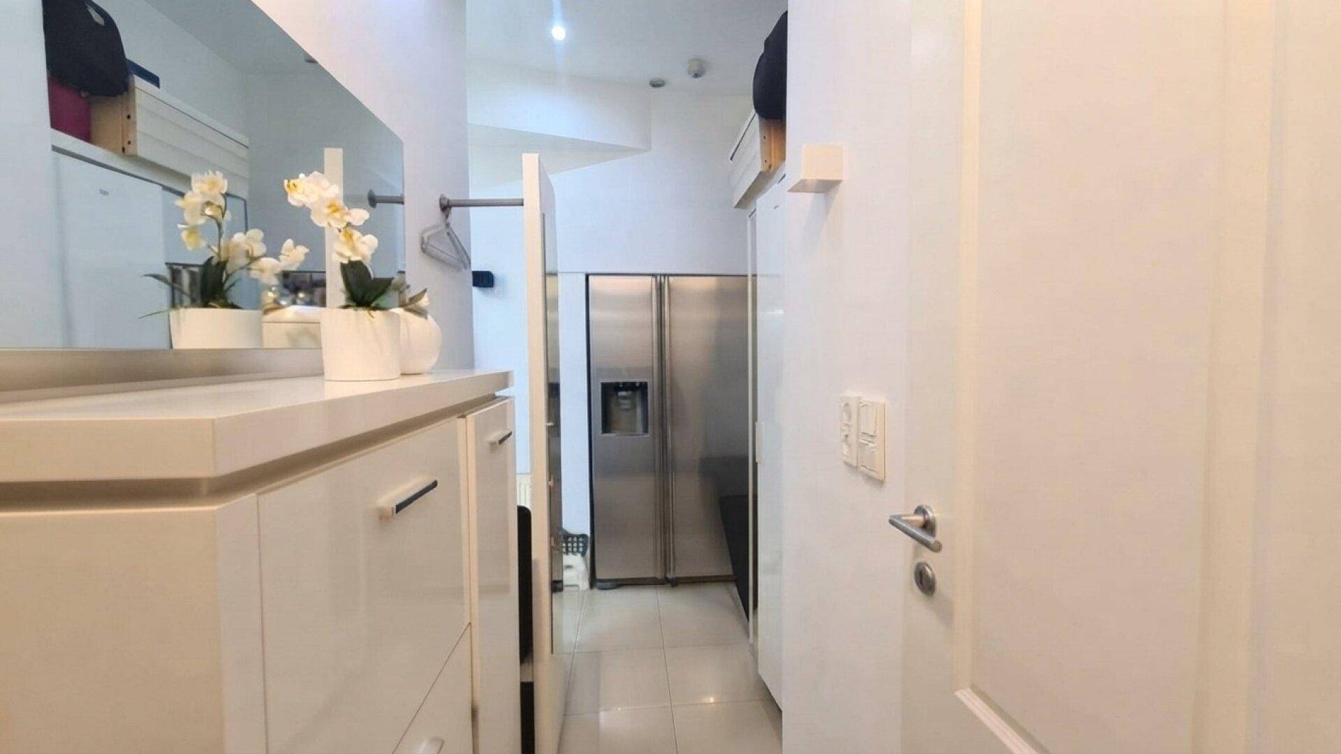 Heller Flur mit weißen Einbauschränken und großem Kühlschrank.