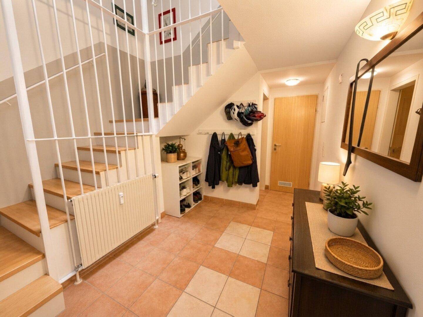 Freundlicher Eingangsbereich mit Holztreppe, Fliesenboden und praktischer Garderobe für den täglichen Gebrauch.