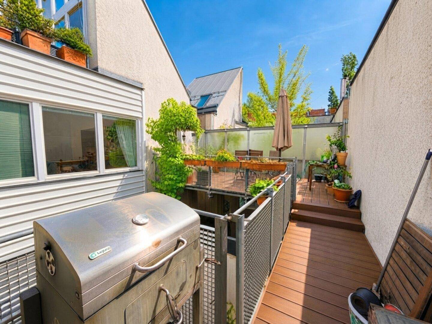 Außenbereich mit Grill und Holzdeck, umgeben von Pflanzen, ideal für gesellige Abende im Freien.