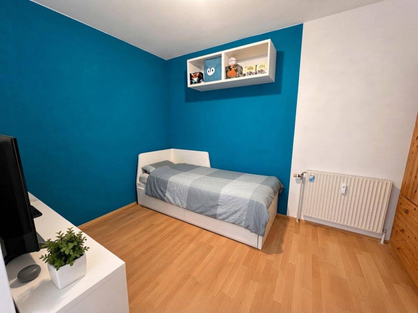 Gemütliches Schlafzimmer mit Einzelbett, blauer Akzentwand und Holzfußboden, ideal für Kinder oder Gäste.