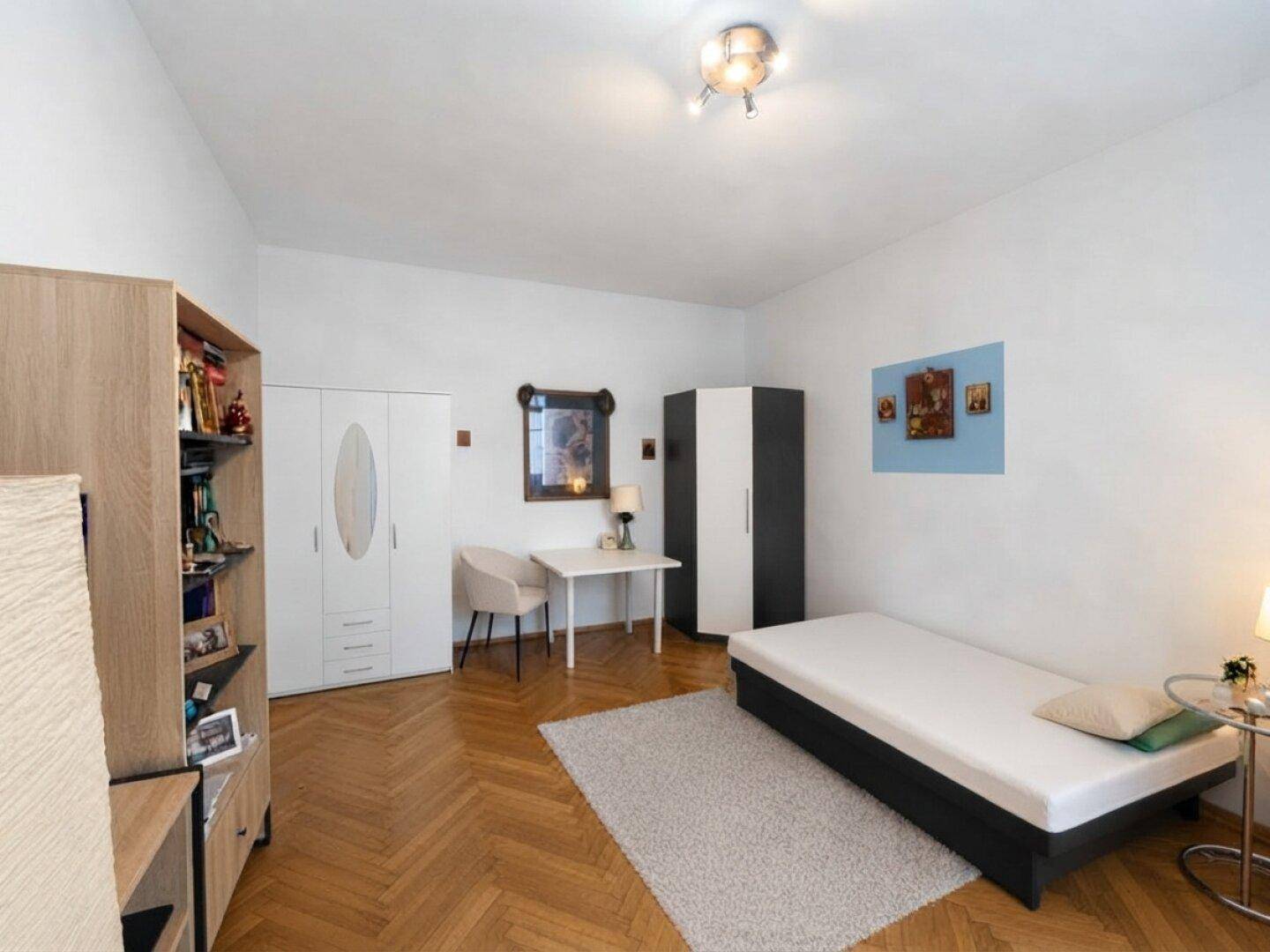 Geräumiges Schlafzimmer mit Einzelbett, Schreibtisch und hellem Fischgrätparkett.