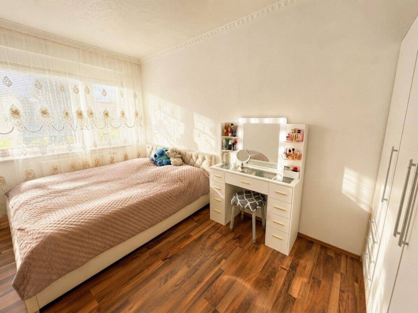 Gemütliches Schlafzimmer mit Holzboden, großem Fenster und modernem Schminktisch.