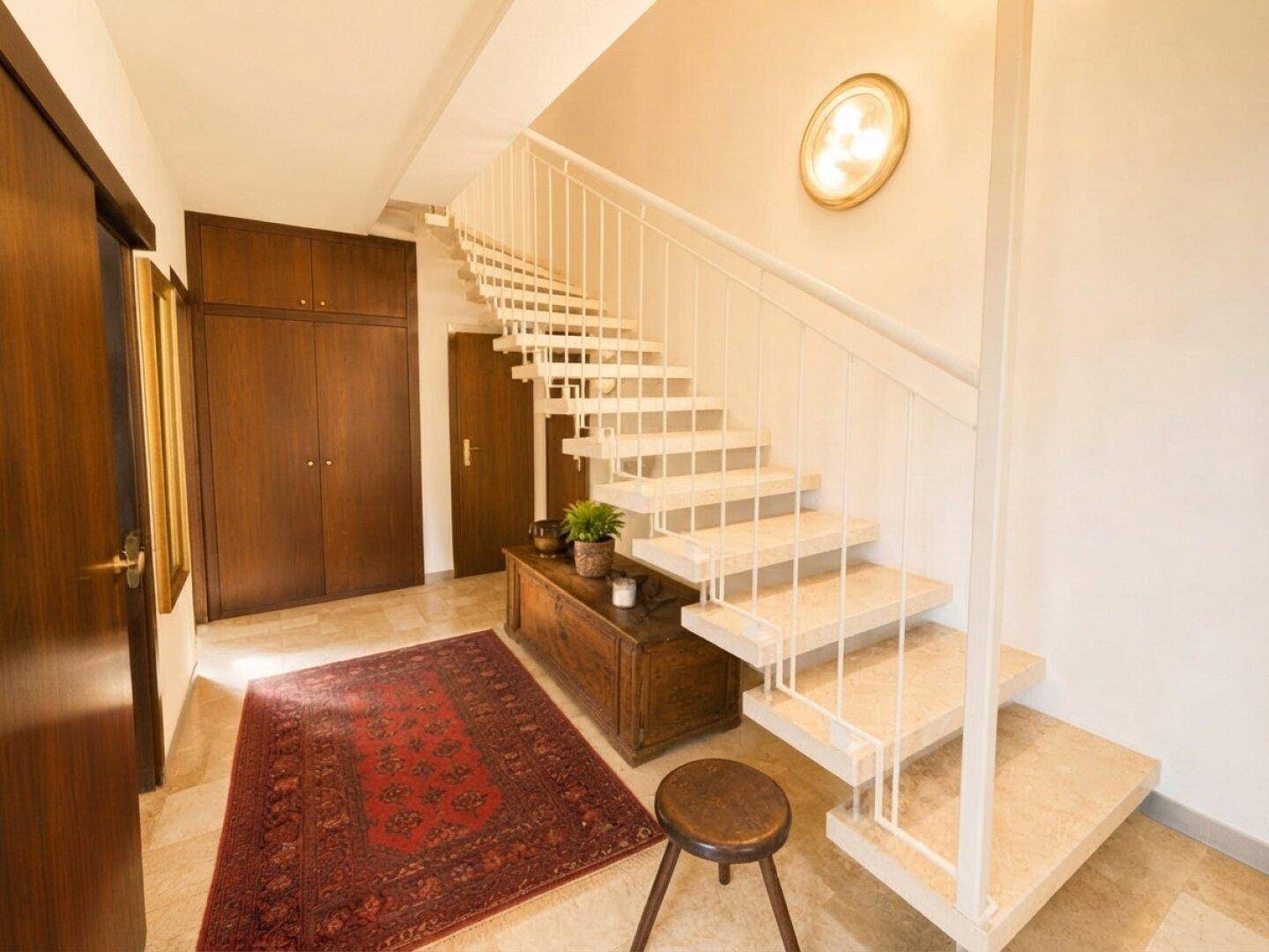 Heller Eingangsbereich mit Steintreppe, Holzschränken und einem dekorativen Teppich.