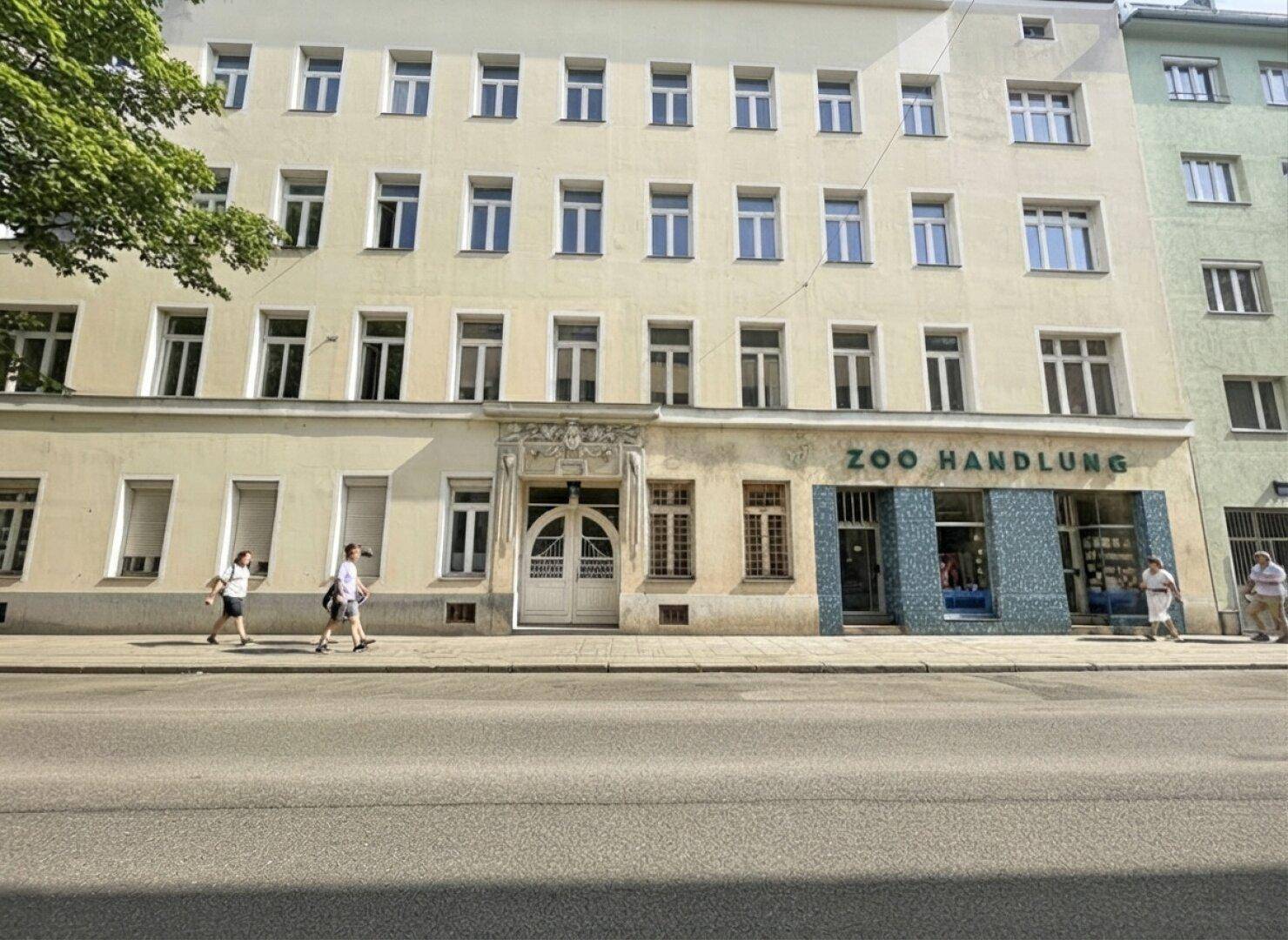 Historische Fassade eines Mehrfamilienhauses mit vielen Fenstern und Geschäftsräumen im Erdgeschoss.