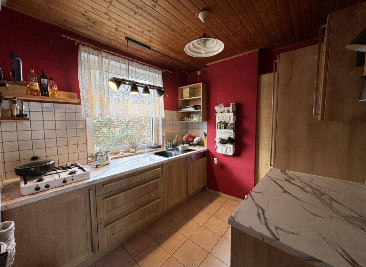 Gemütliche Küche mit roten Wänden, Holzdecke, Gasherd und hellen Holzschränken.