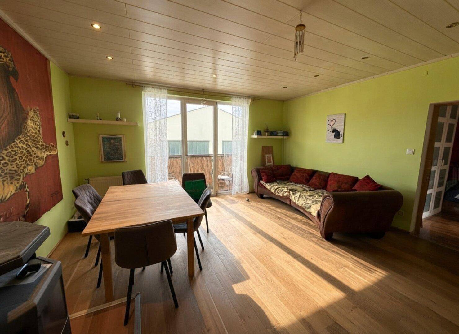 Sonniges Wohn- und Esszimmer mit grün gestrichenen Wänden, Holzboden und Zugang zum Balkon.