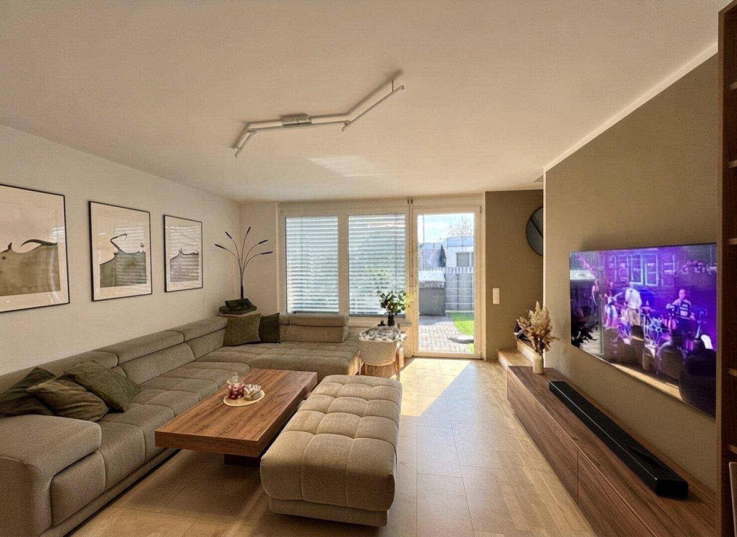 Helles Wohnzimmer mit großem Sofa, Fernseher und direktem Zugang zum Garten.
