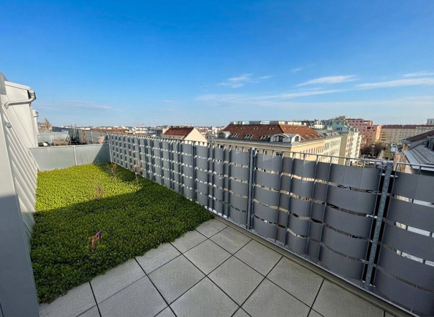 Dachterrasse mit Fliesenboden, Grünfläche und Panoramablick über die Stadt.