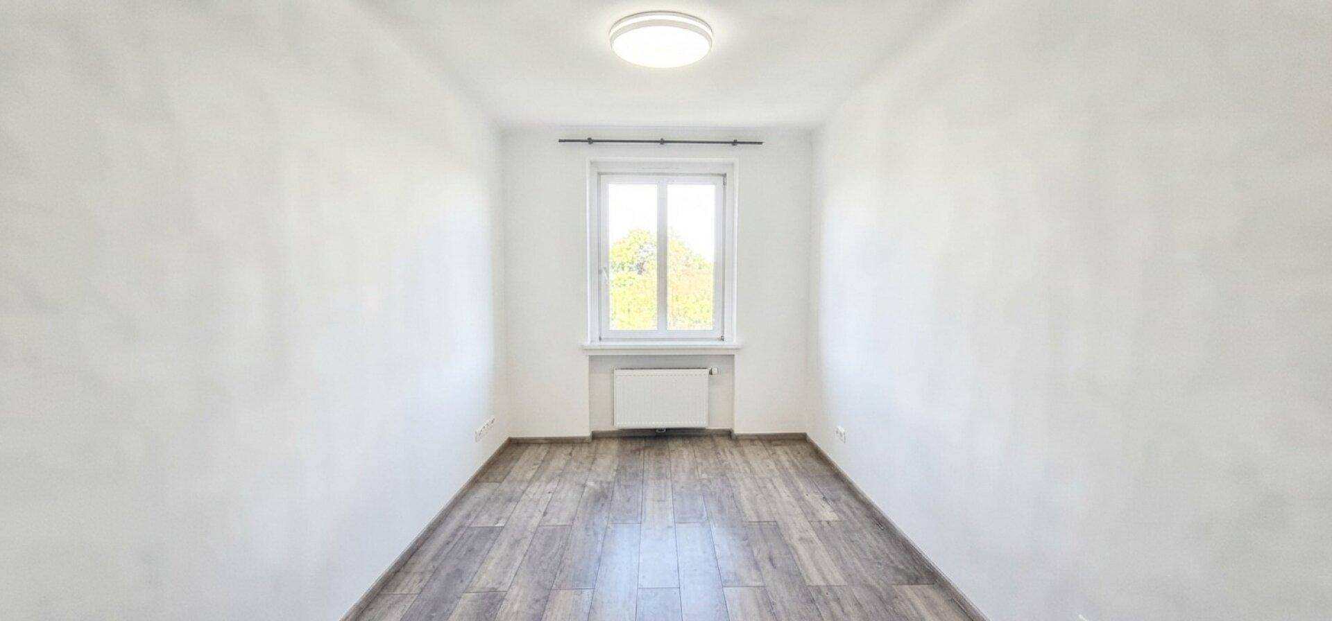 Schmaler, heller Raum mit Laminatboden und einem Fenster, ideal für ein kleines Büro.
