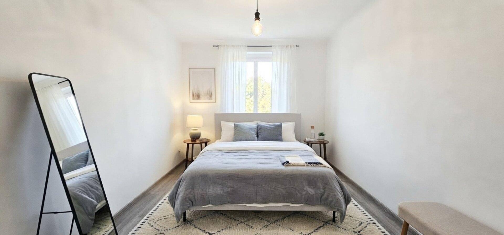 Gemütliches Schlafzimmer mit Doppelbett, großem Spiegel und hellem Fenster.