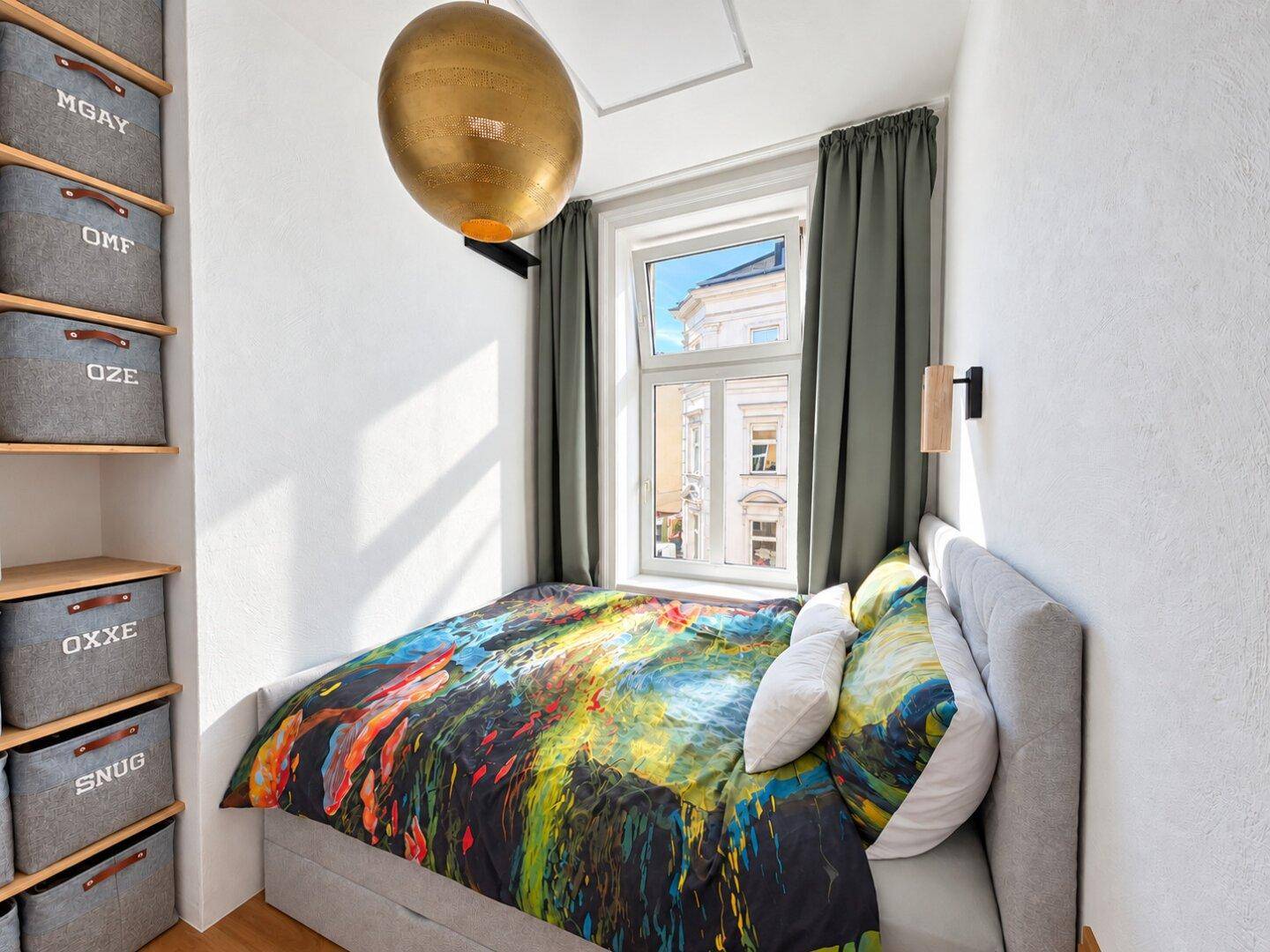 Gemütliches Schlafzimmer mit farbenfroher Bettwäsche, Fenster und praktischen Regalen.