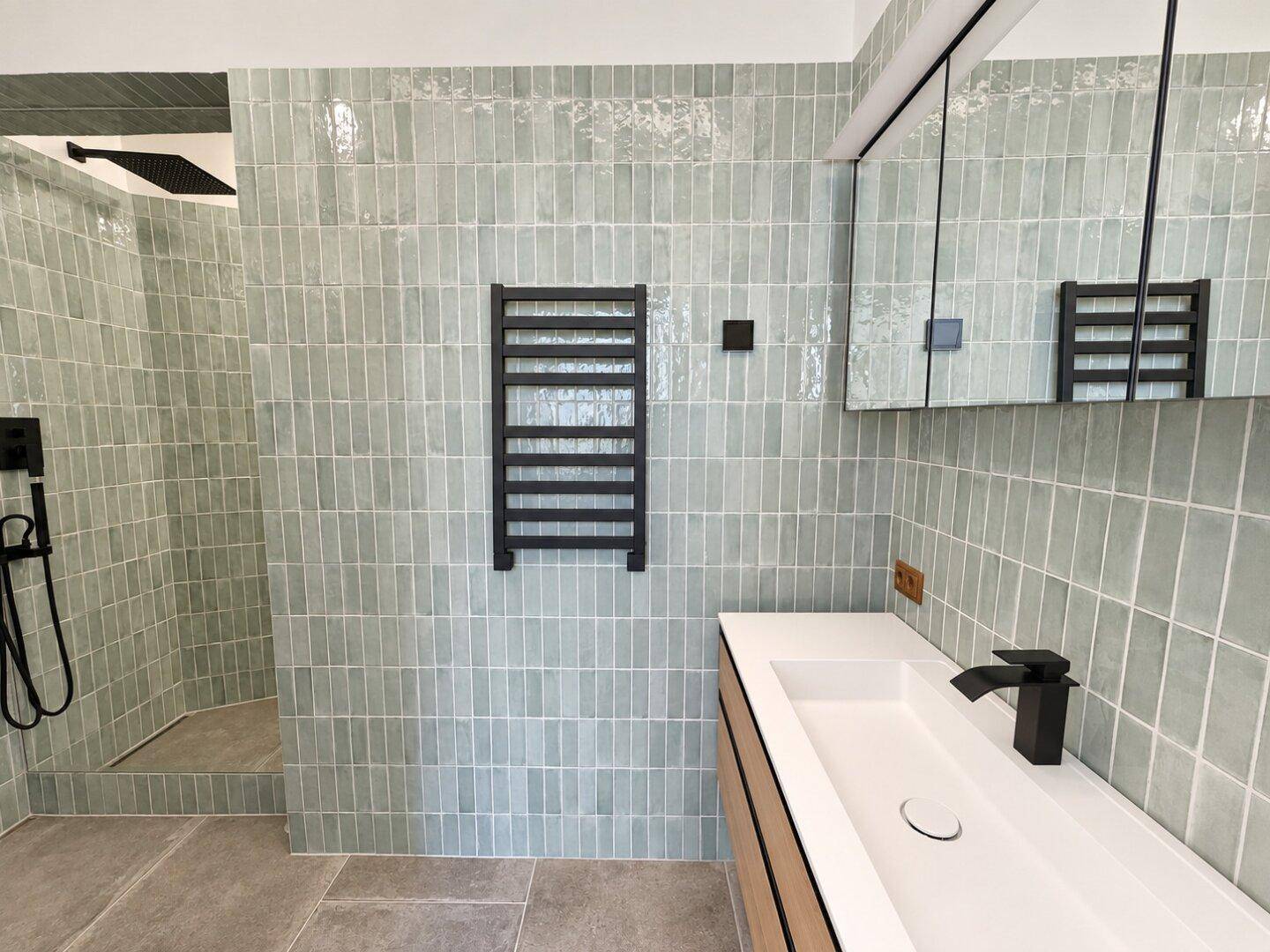 Modernes Badezimmer mit hellgrünen Fliesen, ebenerdiger Dusche und beheiztem Handtuchhalter.