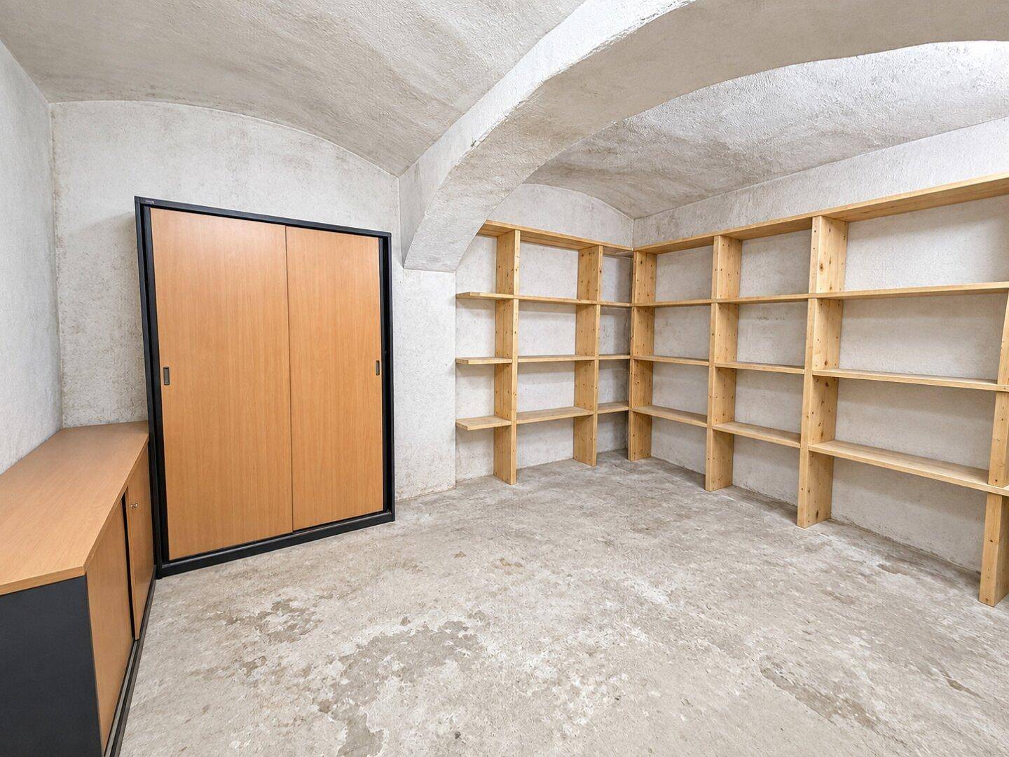 Geräumiger Kellerraum mit Gewölbedecke, Betonboden und praktischen Holzregalen zur Lagerung.