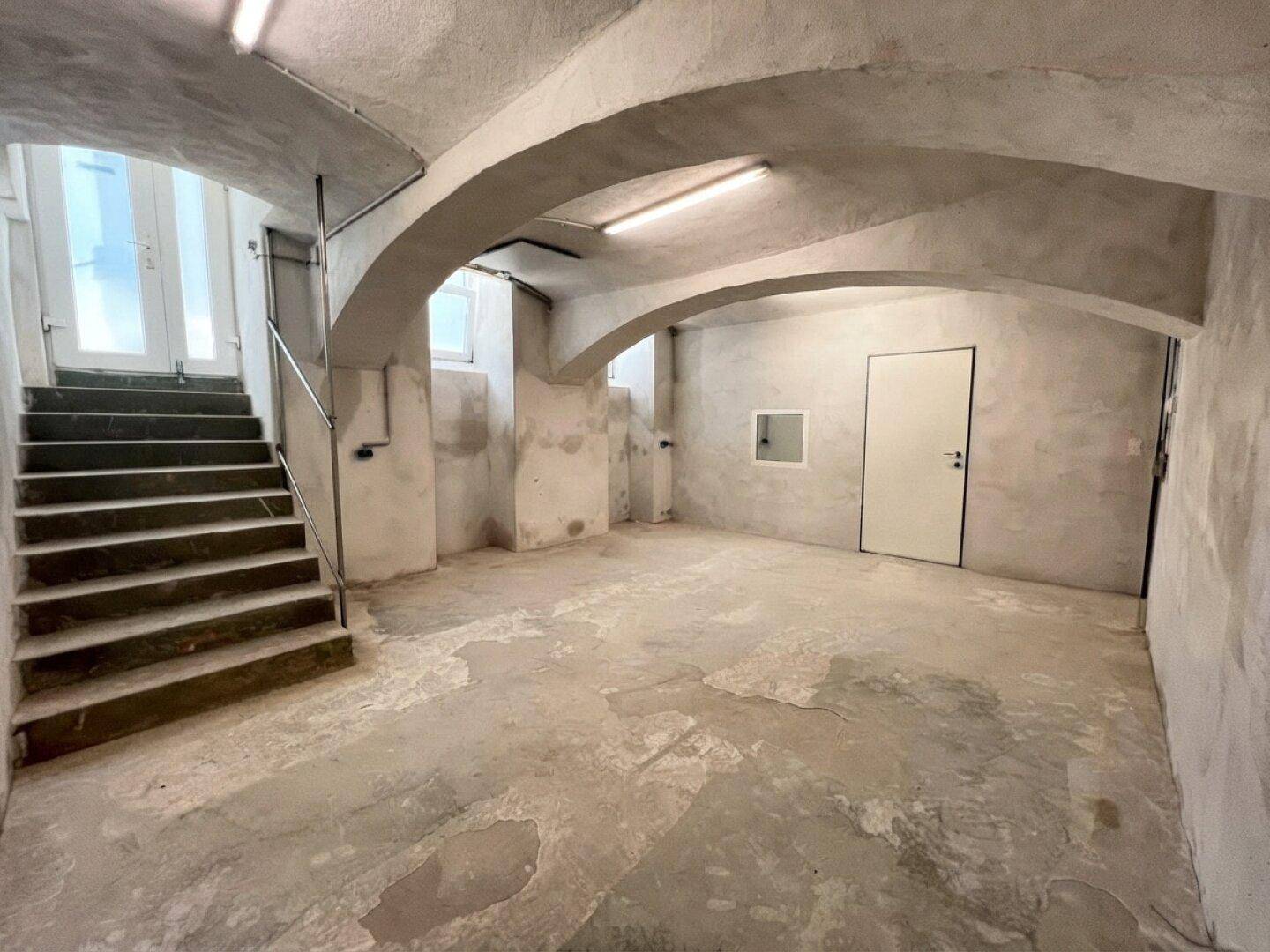 Geräumiger Kellerraum mit Betontreppe, gewölbter Decke und unfertigen Wänden.