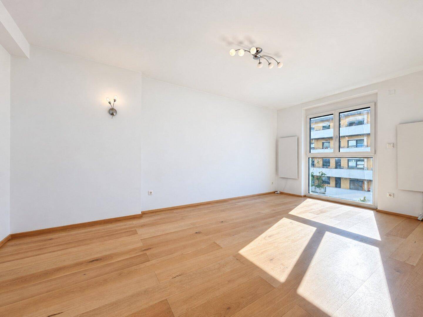 Geräumiges, unmöbliertes Wohnzimmer mit hellem Holzboden und großen Fenstern für viel Tageslicht.