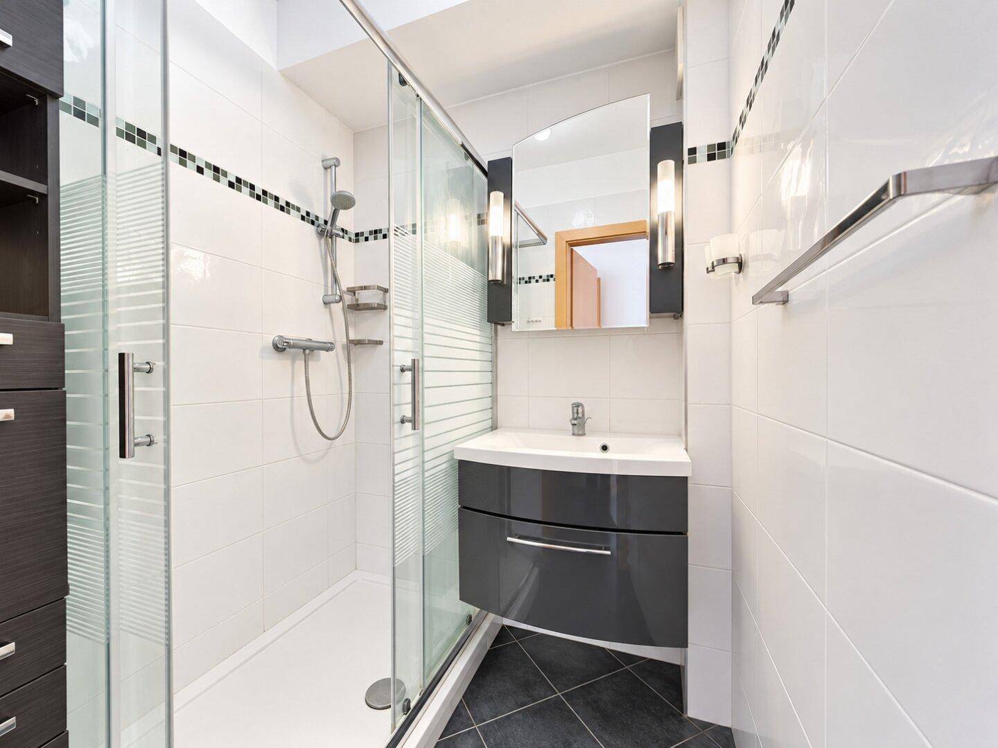 Modernes Badezimmer mit Duschkabine, Waschbecken und Spiegel, ausgestattet mit dunklen Fliesen.