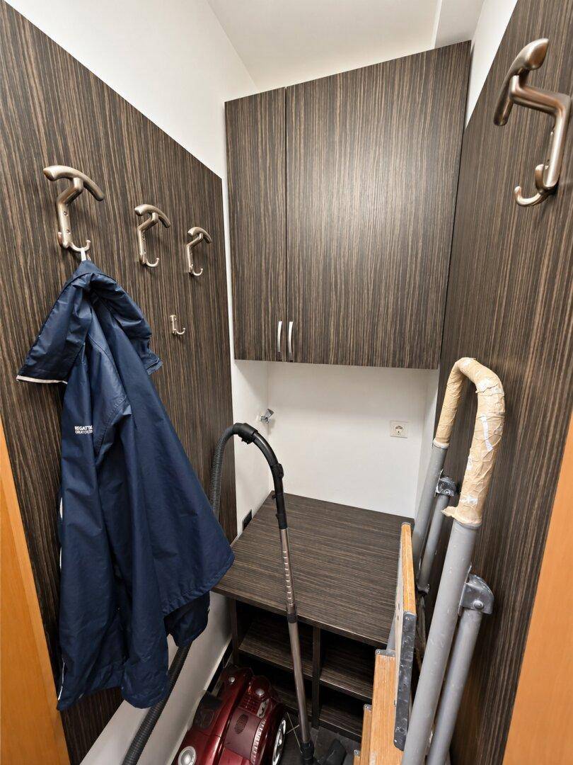 Praktischer Abstellraum mit dunklen Holzpaneelen, Haken und Stauraum für Haushaltsgeräte.