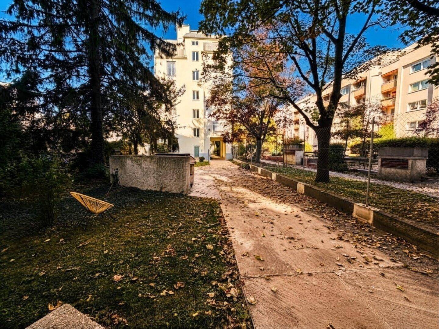 Außenansicht eines Wohngebäudes mit Bäumen und einem Weg, umgeben von Herbstlaub.