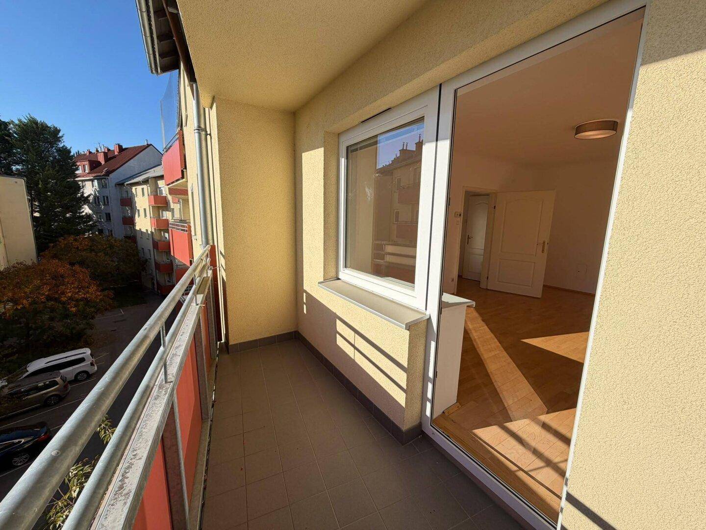 Heller Balkon mit Blick auf die umliegenden Gebäude und Bäume, zugänglich vom Innenraum.