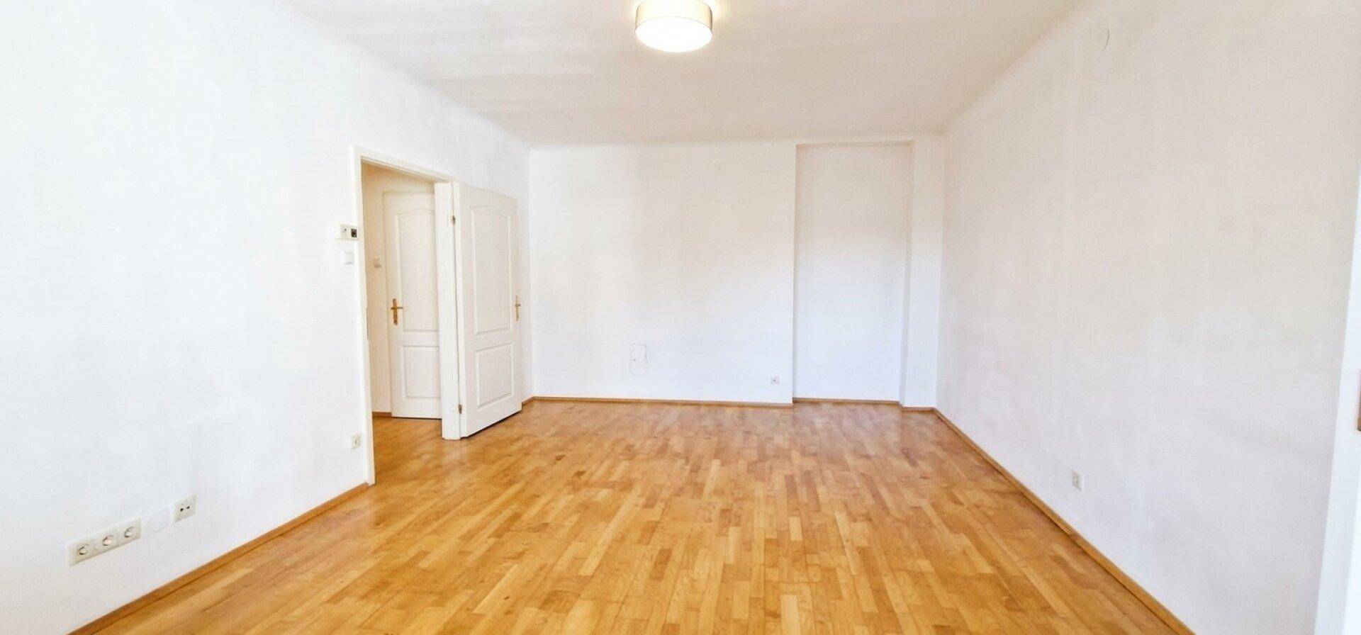Leeres Zimmer mit hellem Parkettboden und weißen Wänden, bereit zur individuellen Gestaltung.