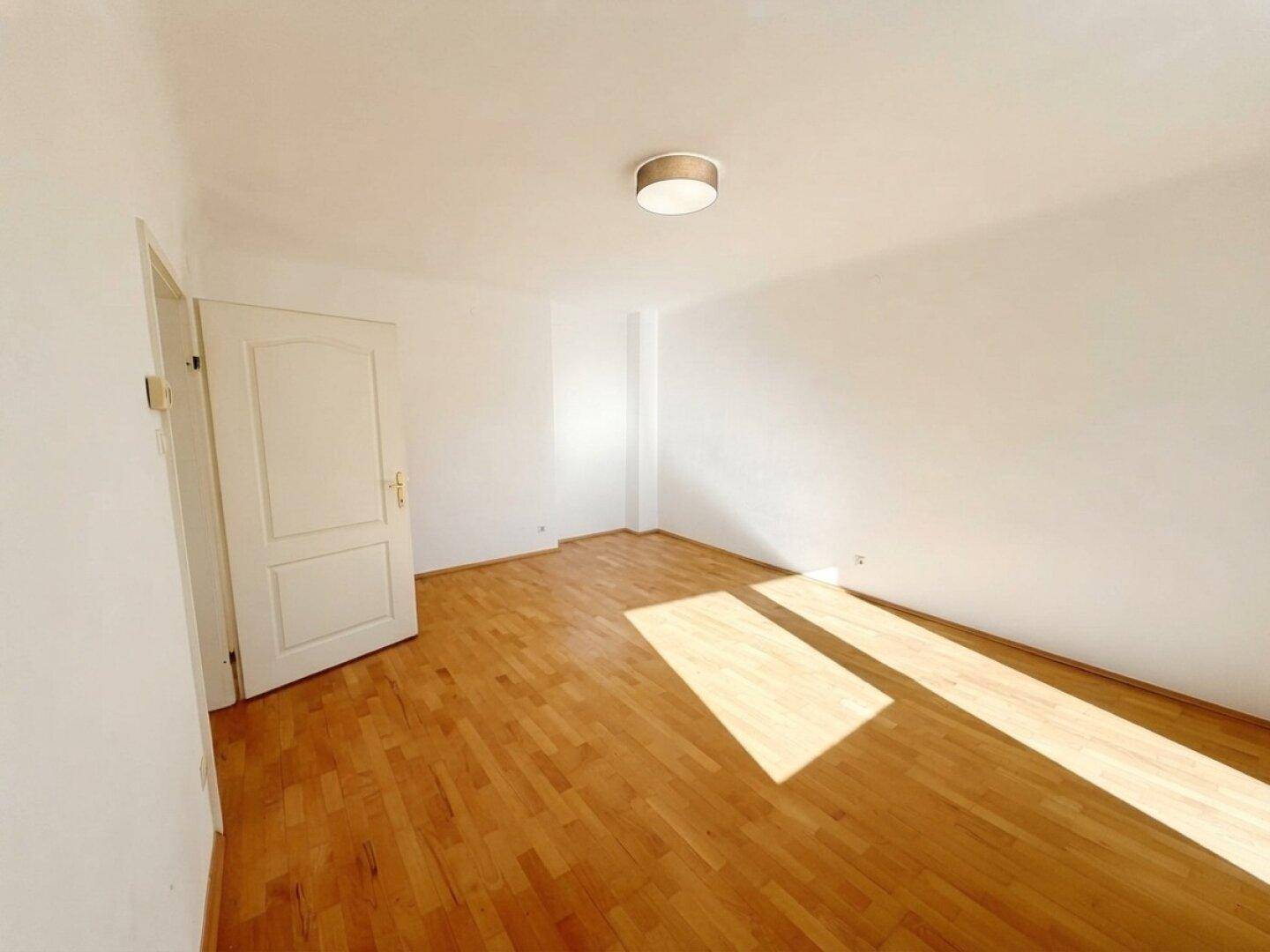 Helles Schlafzimmer mit Parkettboden und weißen Wänden, ideal für individuelle Einrichtung.
