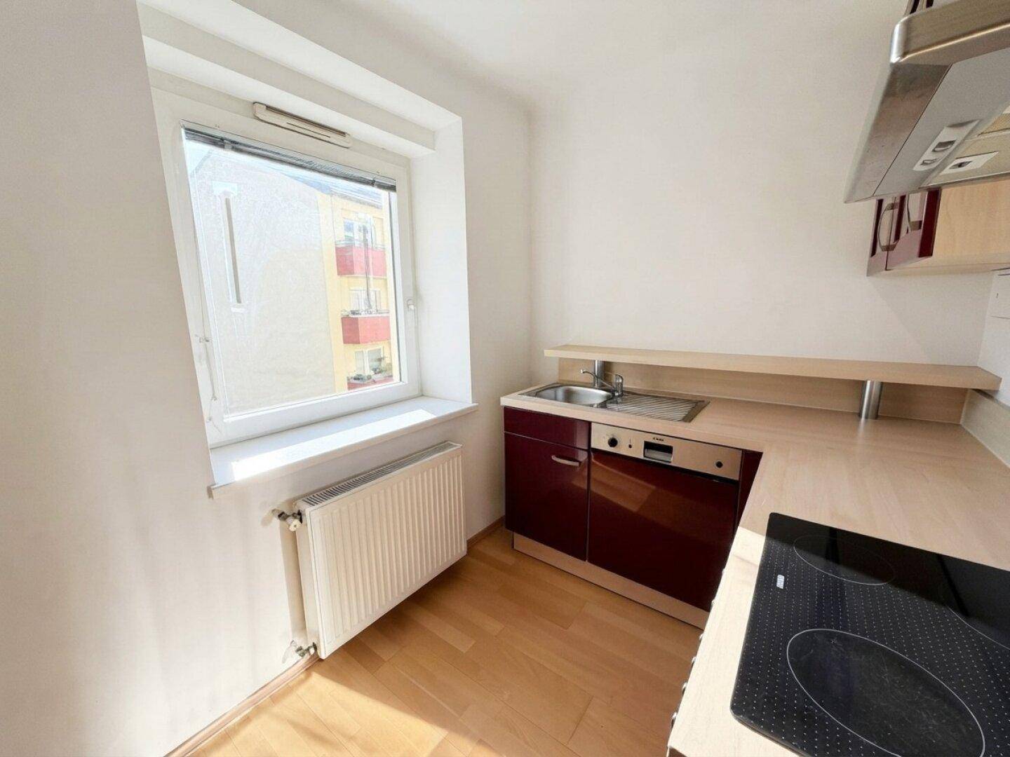 Kompakte Küche mit roten Schränken, Holzarbeitsplatte und Fenster für natürliches Licht.