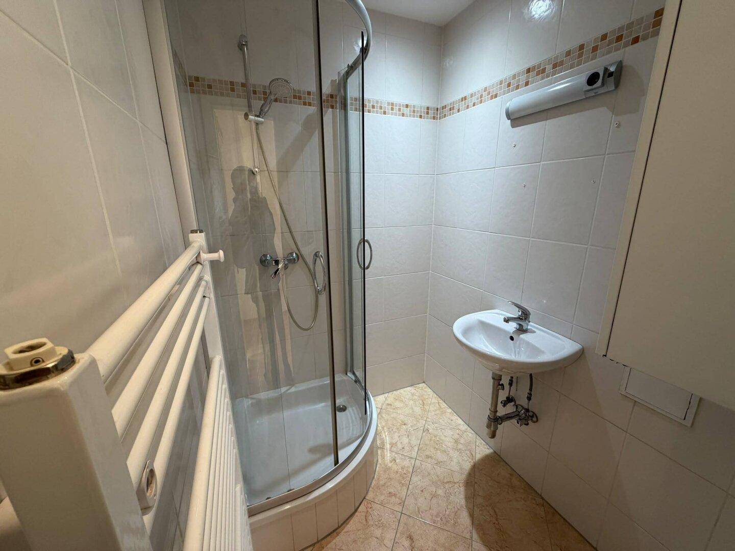 Kleines Badezimmer mit Duschkabine, Waschbecken und beheiztem Handtuchhalter.