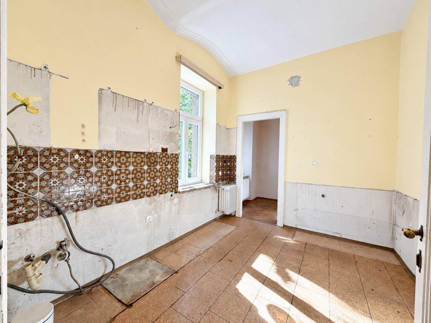 Sanierungsbedürftige Küche mit alten Fliesen und Fenster, bietet Potenzial für eine moderne Neugestaltung.